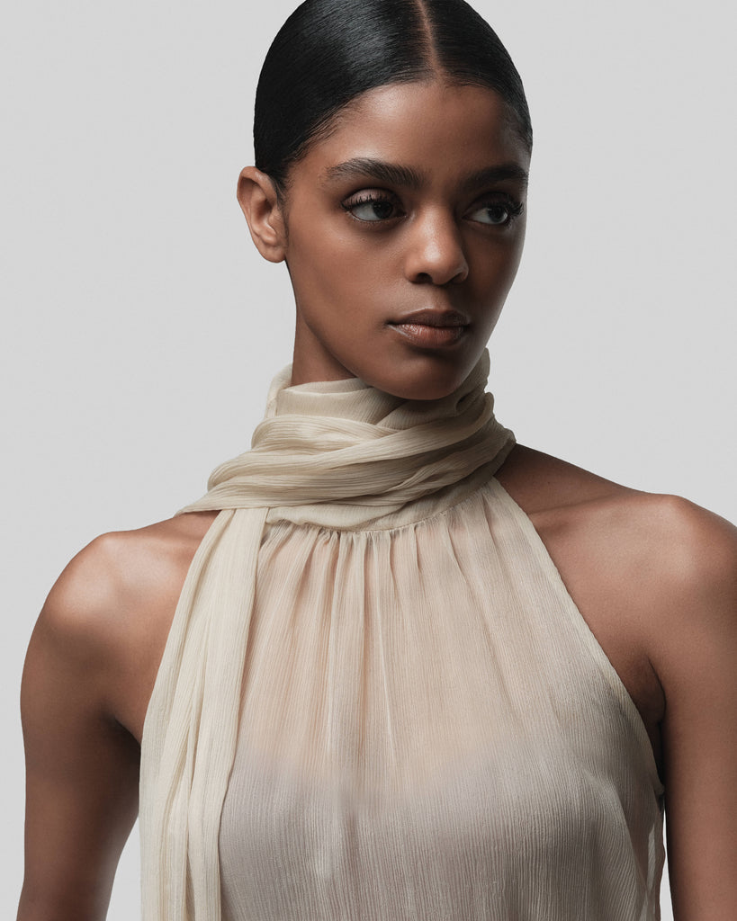 Woman wearing a beige halter top with a matching scarf against a plain background